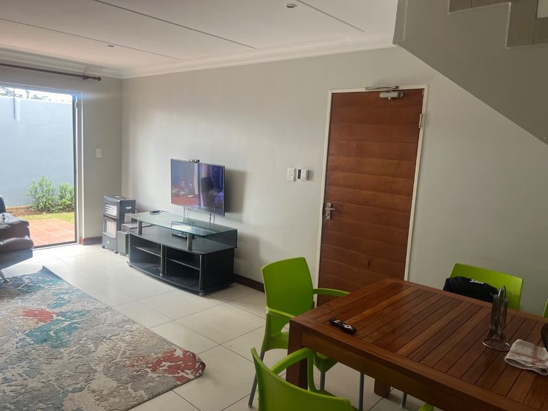 A bright living area featuring tiled floors, recessed lighting, and a solid wood door, with direct access to an outdoor patio area.