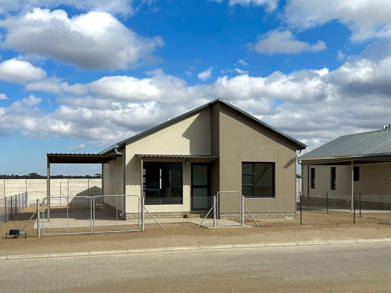A modern single-story detached house featuring a neutral exterior, metal roof, covered carport, and secure perimeter fencing with a gated entrance.