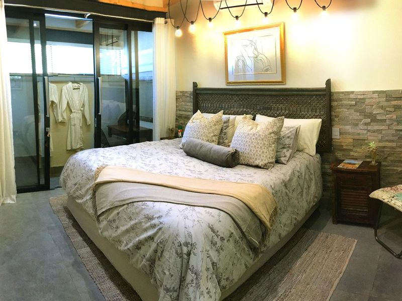 Spacious bedroom featuring a textured stone accent wall, exposed ceiling beams, and large sliding glass doors providing access to an outdoor area.