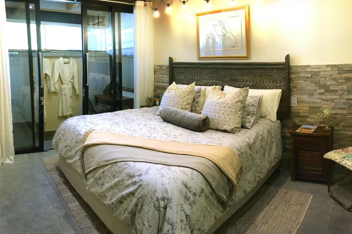 Spacious bedroom featuring a textured stone accent wall, exposed ceiling beams, and large sliding glass doors providing access to an outdoor area.