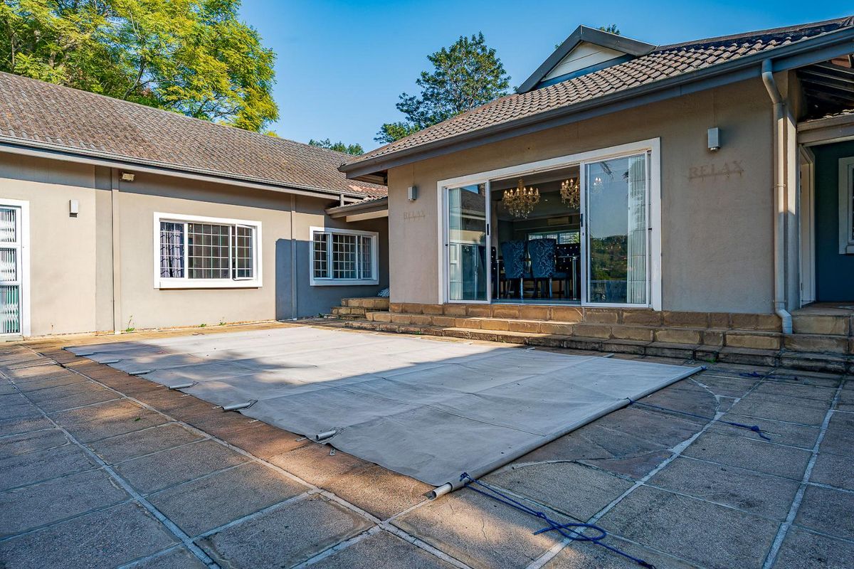 Rear exterior view featuring a paved patio area with a covered swimming pool and sliding glass doors leading into the home.