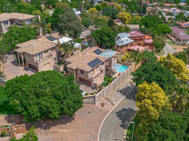Aerial view of a residential property featuring a tiled roof with solar panels, a private swimming pool, and a paved driveway within a suburban estate.