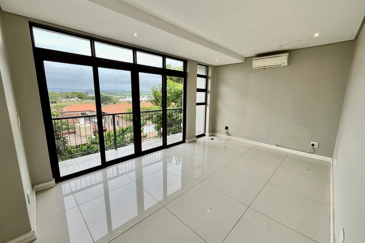 A bright, empty living room featuring large floor-to-ceiling windows, tiled flooring, and a wall-mounted air conditioning unit.