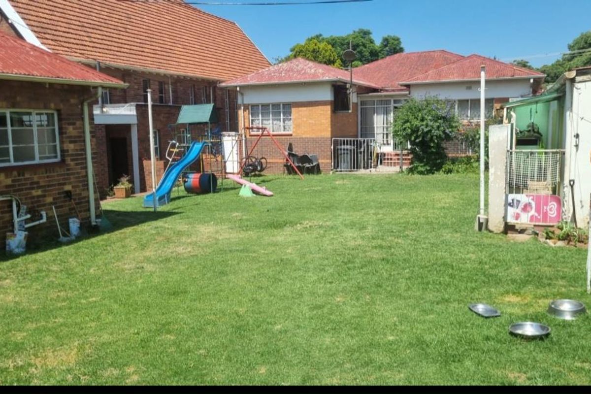 A spacious rear garden area featuring a large lawn, established landscaping, and views of the surrounding brick residential structures.