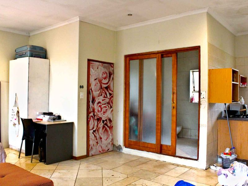 Open plan living area featuring tiled flooring, a sliding timber door leading to a bathroom, and a compact kitchen corner.