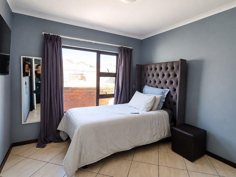 A well-maintained bedroom featuring tiled flooring, neutral blue walls, and a large window providing natural light.