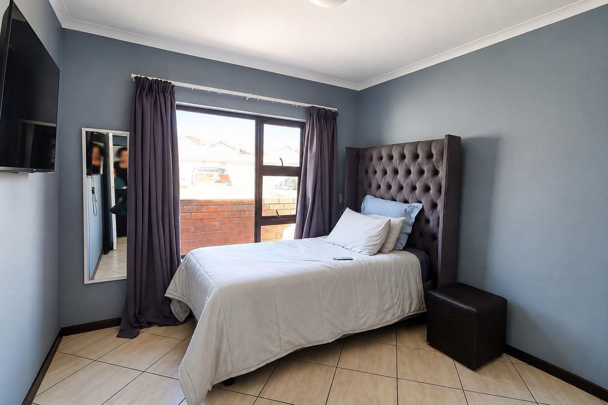 A well-maintained bedroom featuring tiled flooring, neutral blue walls, and a large window providing natural light.