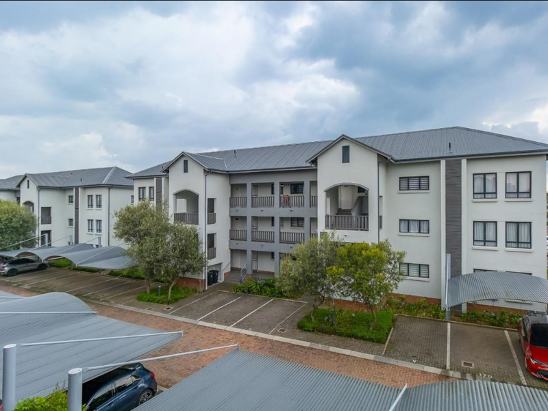 An elevated view of a modern apartment complex featuring multi-level units with balconies, covered parking bays, and well-maintained paved grounds.