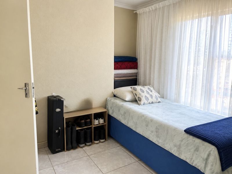 A functional bedroom featuring tiled flooring and large windows with curtains, providing a bright and practical living space.