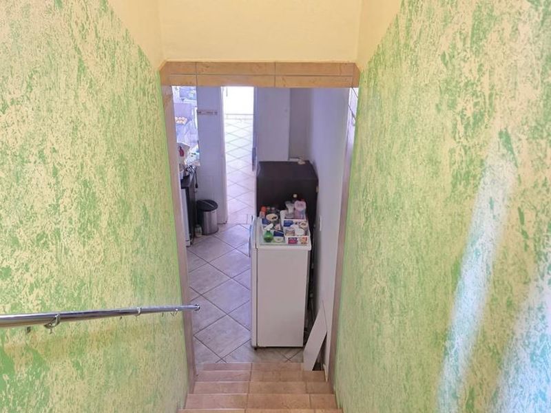 A staircase with tiled steps and a metal handrail, leading down to a lower level area with tiled flooring.