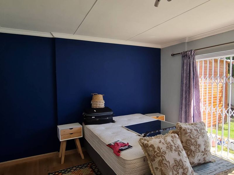 Bedroom featuring laminate flooring, built-in cupboards, and a sliding glass door with a security gate providing direct access to the garden.