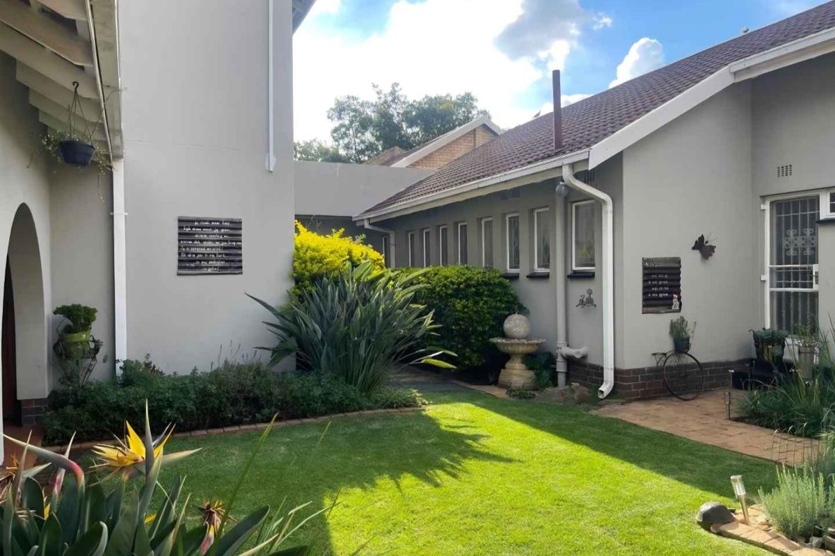 A well-maintained rear garden area featuring a manicured lawn, established landscaping, and paved pathways adjacent to the house exterior.