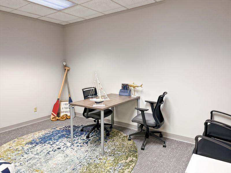 A functional office space featuring neutral walls, carpet flooring, and a suspended ceiling with recessed lighting, suitable for a professional work environment.