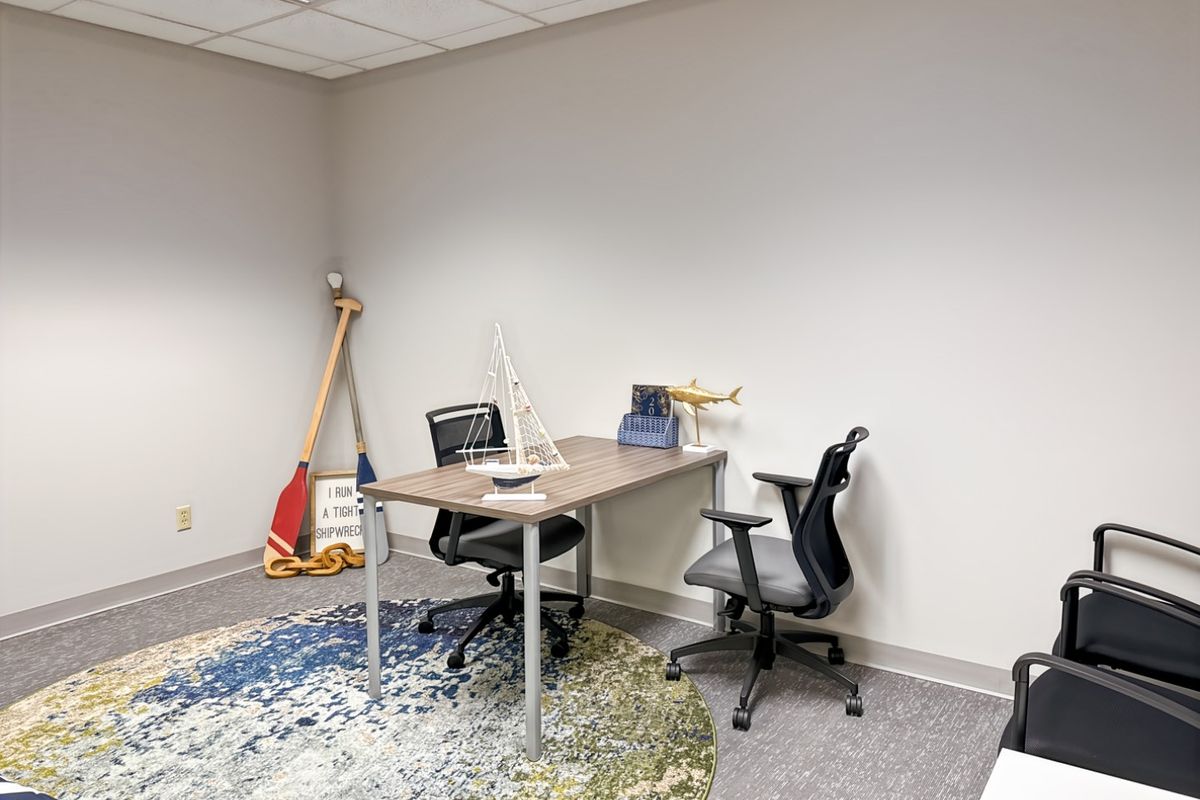 A functional office space featuring neutral walls, carpet flooring, and a suspended ceiling with recessed lighting, suitable for a professional work environment.