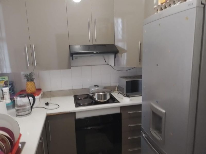 Compact kitchen featuring modern high-gloss cabinetry, built-in oven, electric hob, extractor fan, and tiled backsplash with ample counter space.
