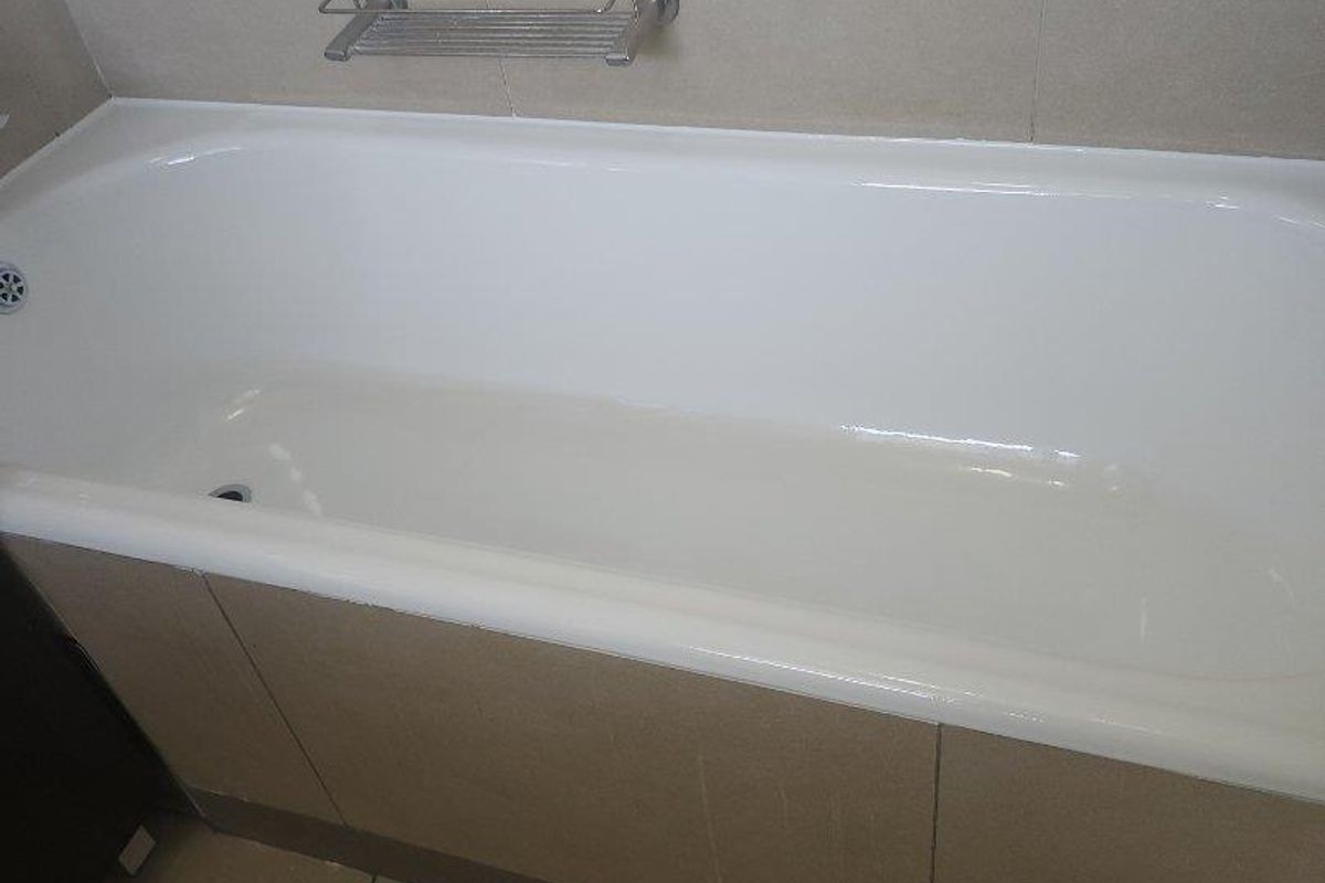 A clean, neutral-toned bathroom featuring a built-in bathtub with tiled surround and wall-mounted metal soap dish.