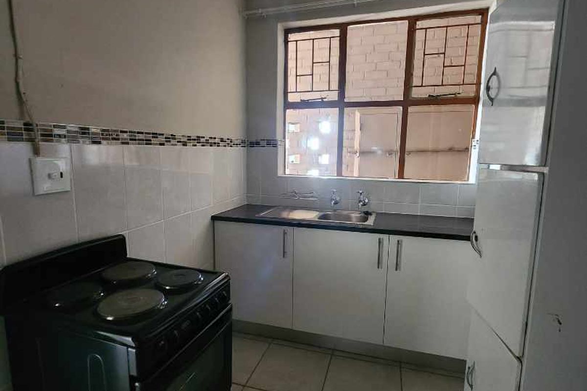 A functional kitchen featuring tiled flooring, built-in cabinetry, a stainless steel sink, and a freestanding stove.