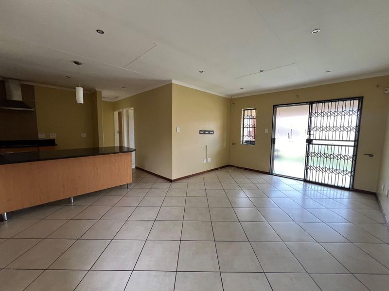 Spacious open-plan living area featuring tiled floors, a kitchen island with granite countertops, and direct access to the exterior through a sliding security door.