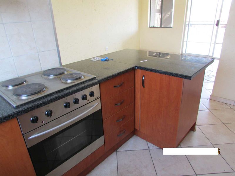 A functional kitchen area featuring granite countertops, built-in oven and hob, wooden cabinetry, and tiled flooring with access to an outdoor balcony.