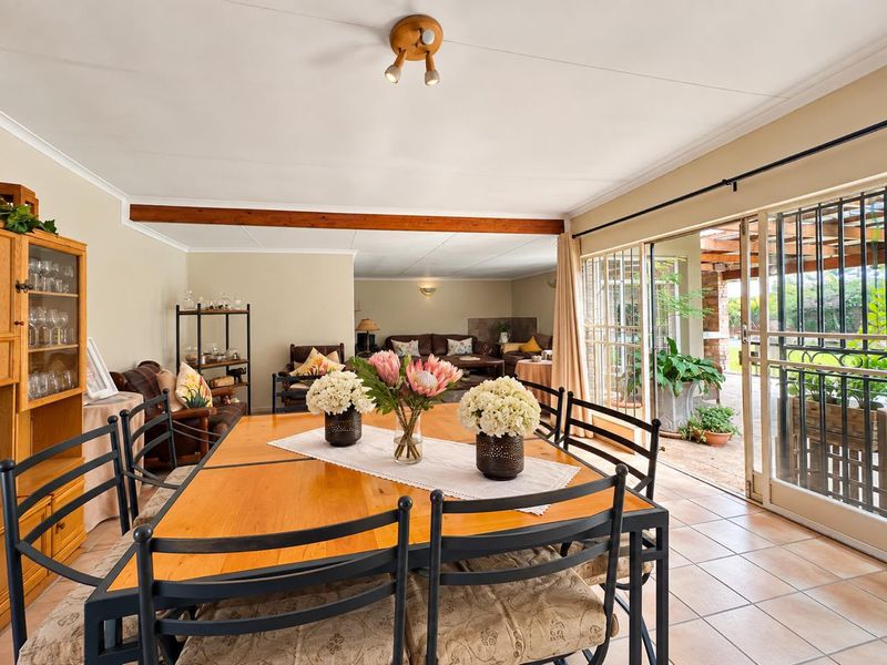 Spacious open-plan dining and living area featuring tiled floors, an exposed timber beam, and large sliding doors providing seamless access to the outdoor patio.