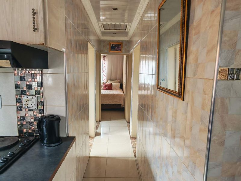 A compact kitchen area featuring tiled walls and flooring, leading into a hallway with a view of an adjacent bedroom.