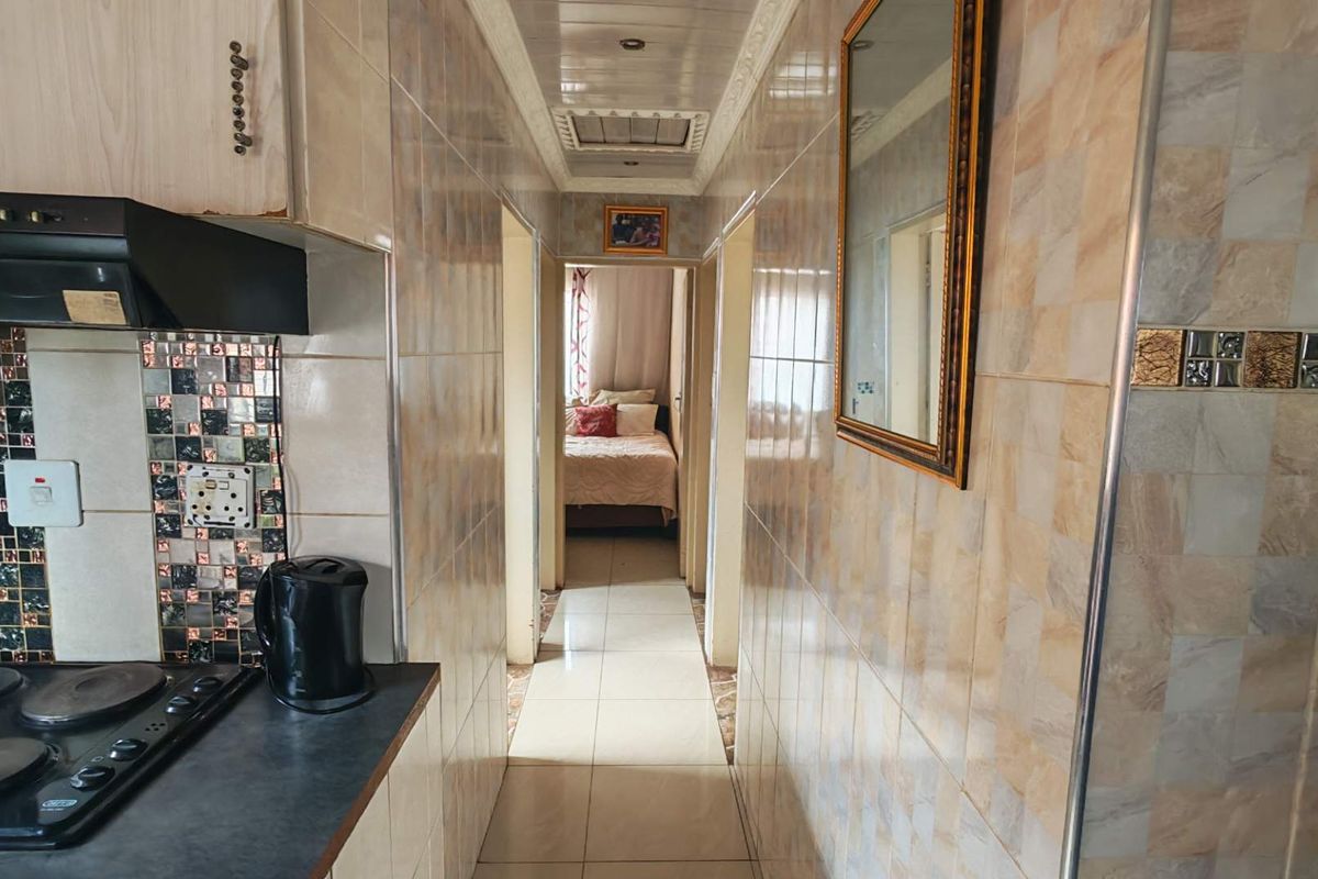 A compact kitchen area featuring tiled walls and flooring, leading into a hallway with a view of an adjacent bedroom.