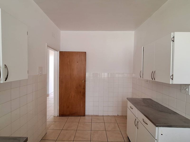A functional, empty kitchen featuring white built-in cabinetry, tiled backsplash, and tiled flooring, offering a blank canvas for potential renovation or modernization.