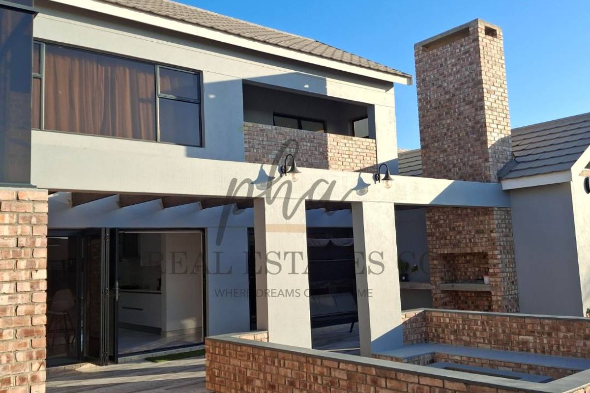 Rear exterior view featuring a paved patio, built-in brick fireplace, and covered outdoor entertainment area with modern architectural finishes.