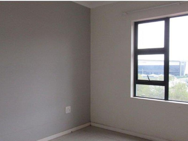An empty bedroom featuring neutral painted walls, tiled flooring, and a large aluminium-framed window providing natural light.