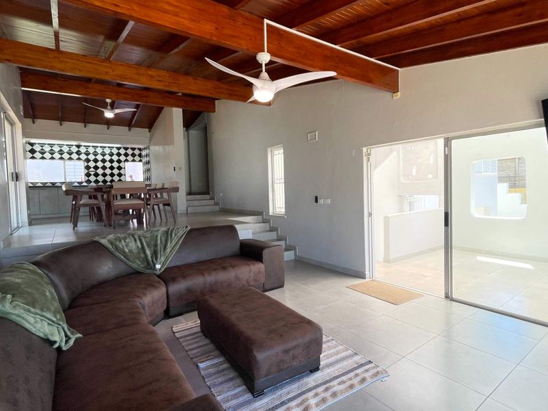 Spacious open-plan living area featuring exposed timber ceiling beams, tiled flooring, and seamless access to an outdoor patio through sliding glass doors.