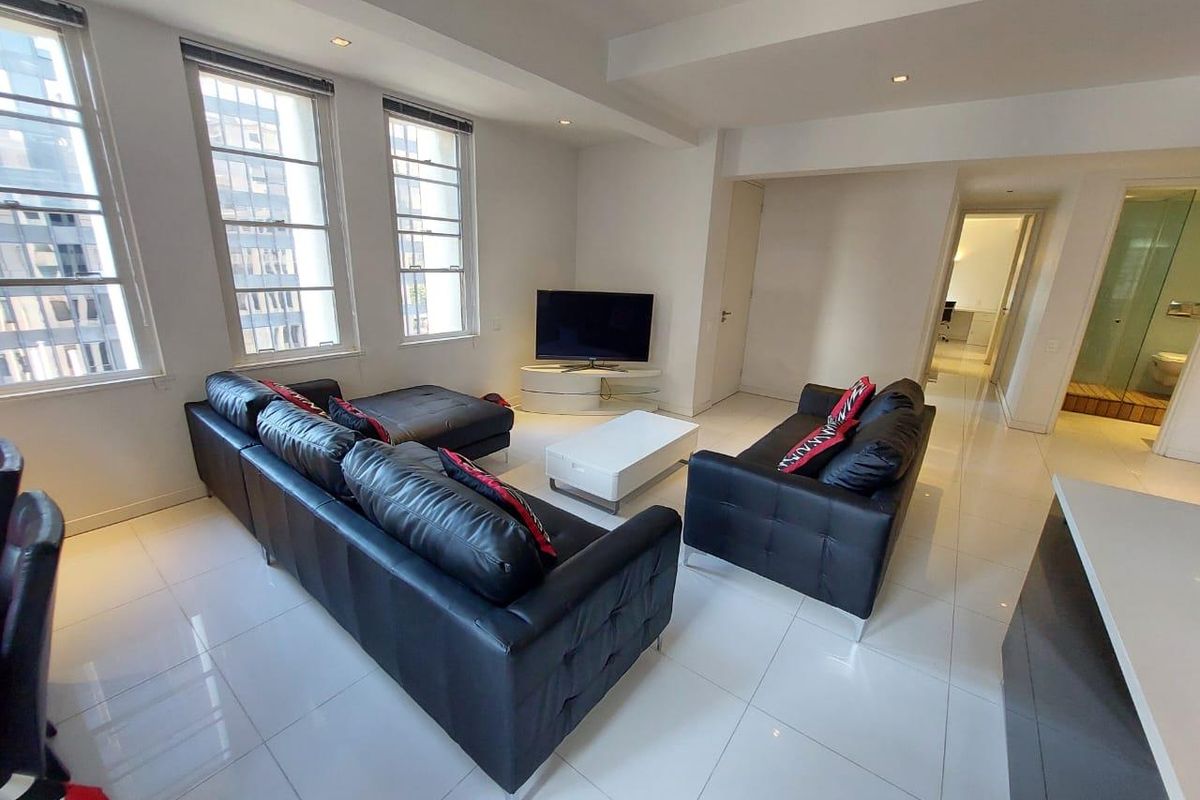 A bright living room featuring large multi-pane windows, polished tiled flooring, and recessed downlighting, offering a clean and neutral base for interior design.