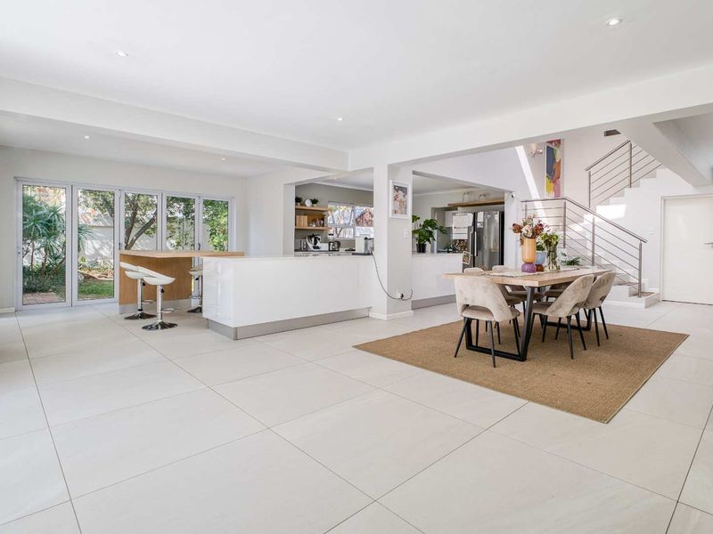 Spacious open-plan living and dining area featuring a modern kitchen island, sleek tiled flooring, and a staircase with a contemporary metal railing.