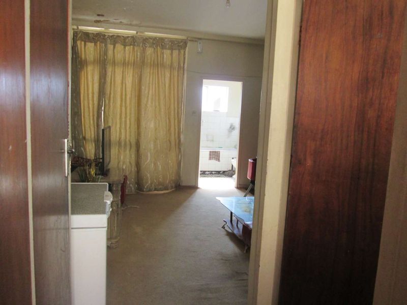 A view into a living area featuring carpet flooring and a sliding glass door, showing signs of ceiling damage and general wear.