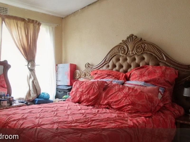 A bedroom featuring a large window with curtains and a ceiling air vent, showing signs of wear on the walls and ceiling.
