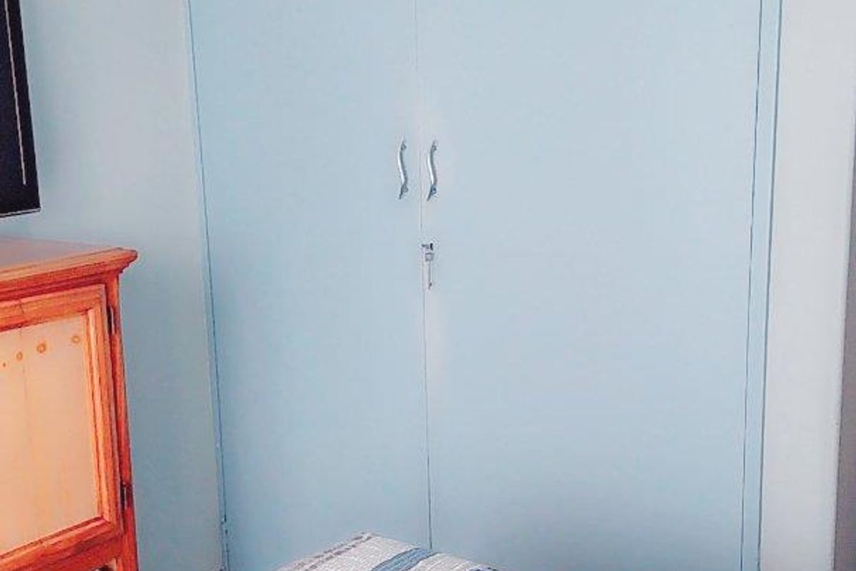 A bedroom featuring a light blue built-in wardrobe with overhead storage compartments.