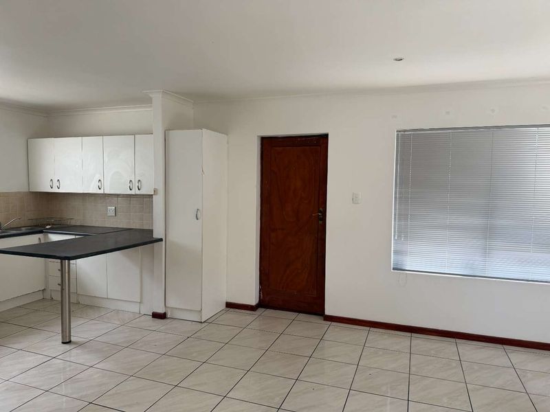 Open plan kitchen and living area featuring tiled flooring, built-in cabinetry with laminate countertops, and a timber door leading to an adjacent space.