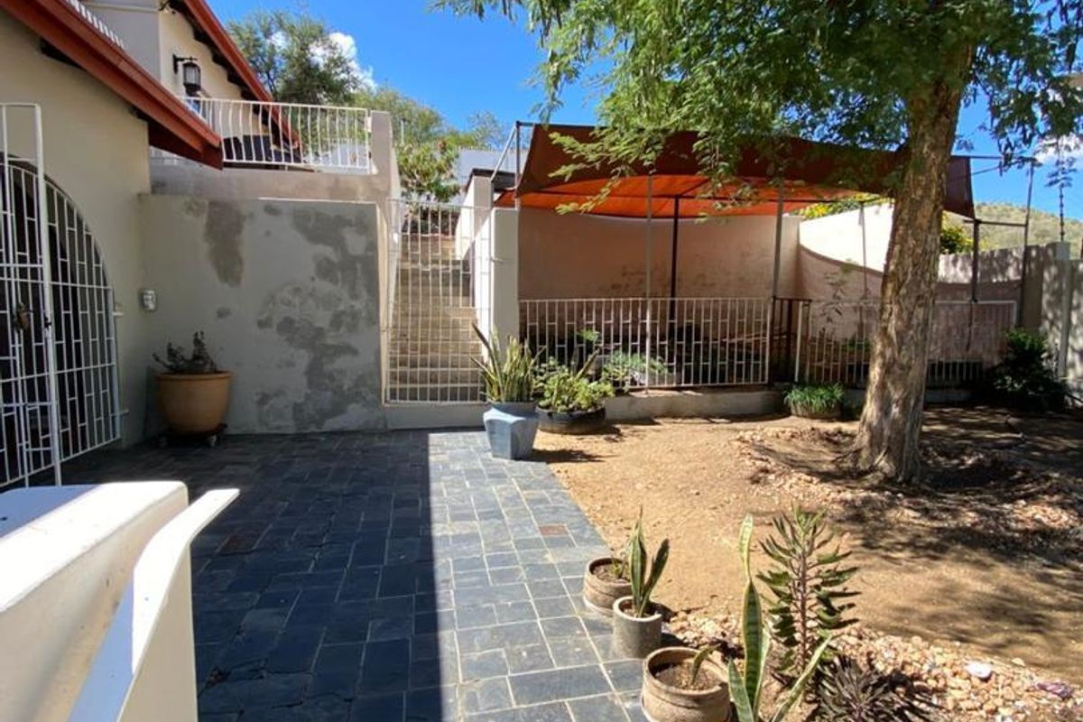 Rear garden area featuring slate paving, a shaded patio space, and tiered levels with metal security gates and balustrades.