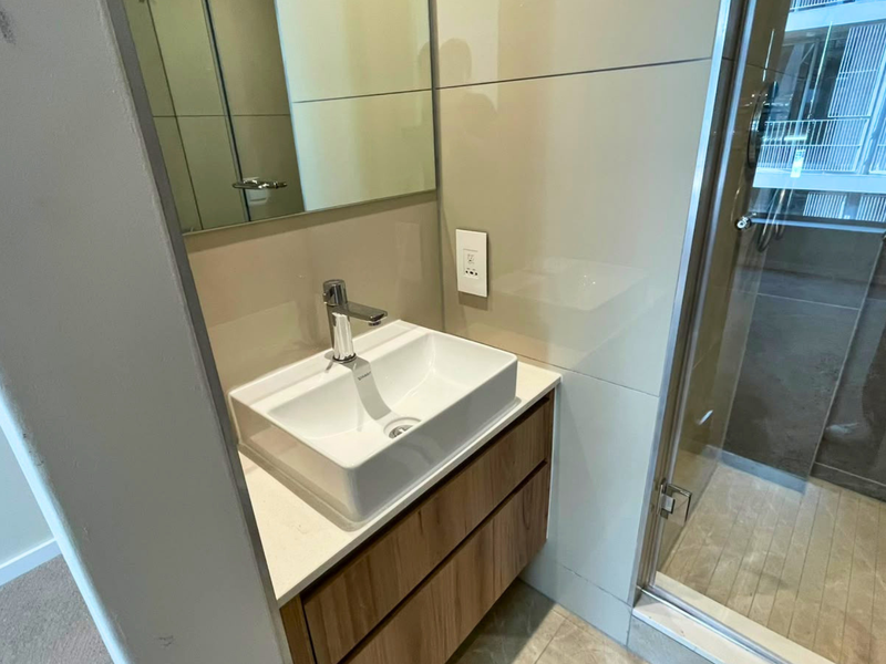 Modern bathroom featuring a vessel sink on a wood-finish vanity, stone countertop, wall-mounted mirror, and a glass-enclosed shower with tiled walls.