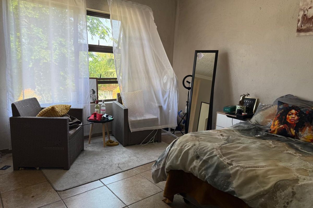 A bedroom featuring tiled flooring and a large window allowing natural light, providing a functional space for rest and relaxation.