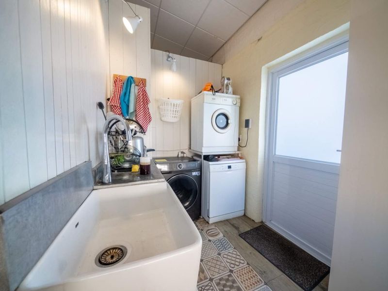 Functional laundry room featuring a classic ceramic butler sink, patterned tiled flooring, and direct access to the exterior.