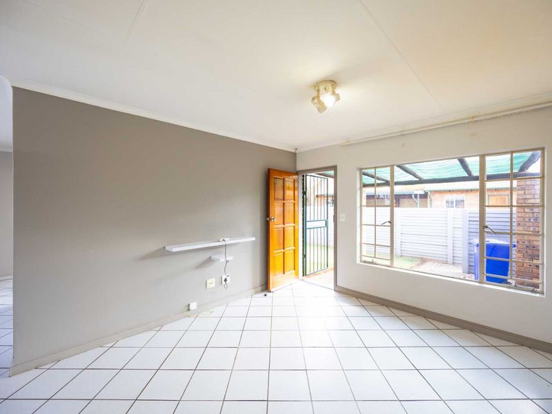 An empty living room featuring tiled flooring, a timber entrance door, and a large window overlooking the rear exterior area.
