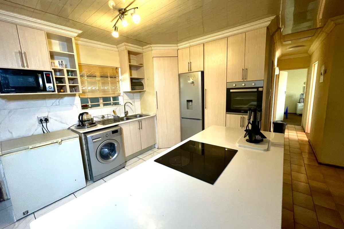 A functional kitchen featuring light wood cabinetry, a central island with an integrated hob, built-in oven, and tiled flooring.