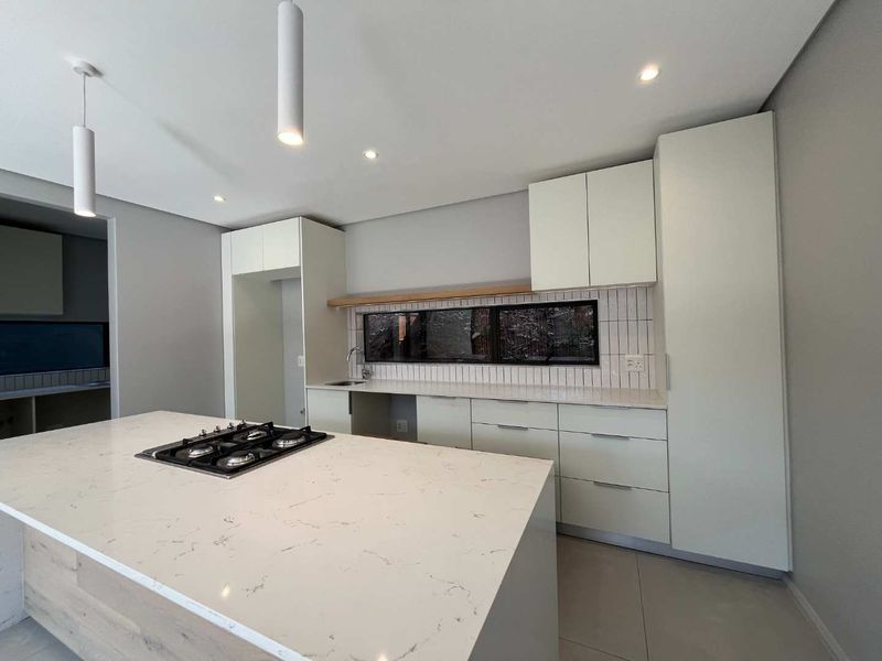 Modern kitchen featuring a central island with a gas hob, stone countertops, sleek cabinetry, and a stylish subway tile backsplash.