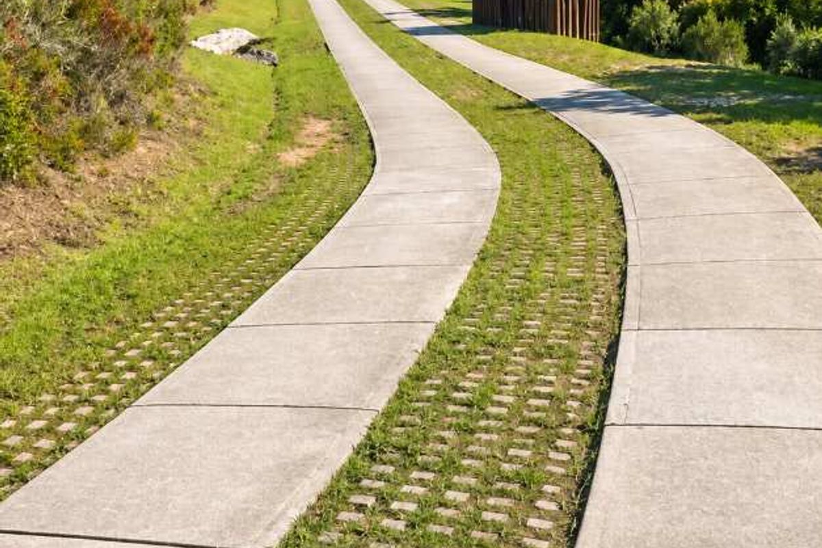 A winding concrete driveway with integrated grass pavers leading through a landscaped residential property with natural hillside surroundings.