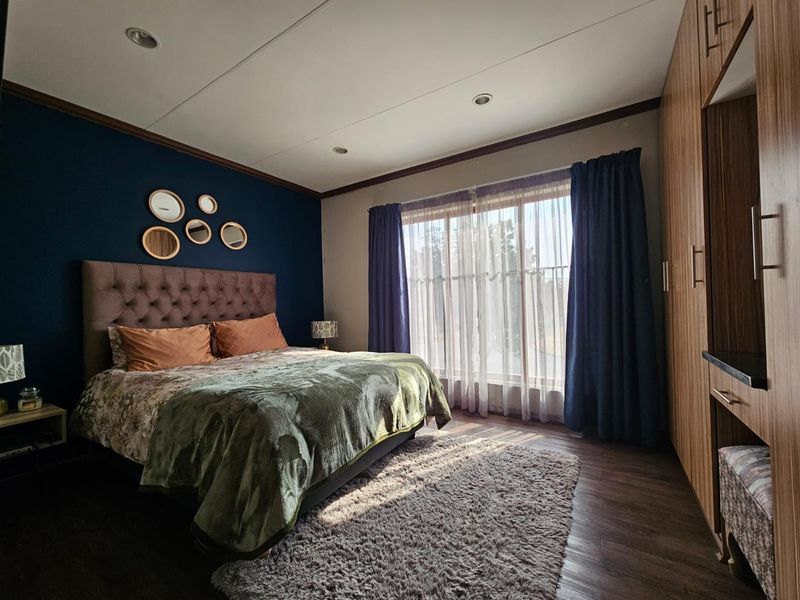 A well-lit bedroom featuring dark blue accent wall, built-in wooden cabinetry, and laminate flooring with large window providing natural light.