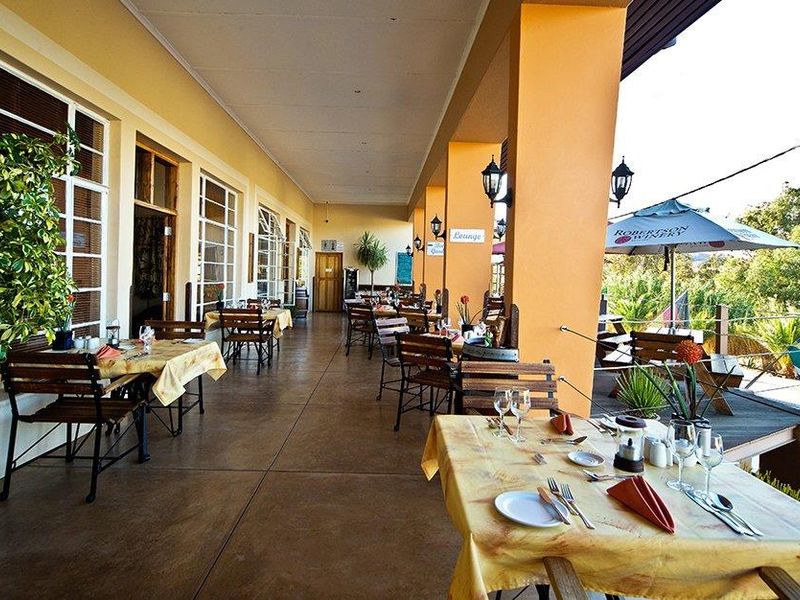 A spacious covered hotel veranda featuring concrete flooring and structural pillars, providing an inviting outdoor dining area with views of the surrounding landscape.