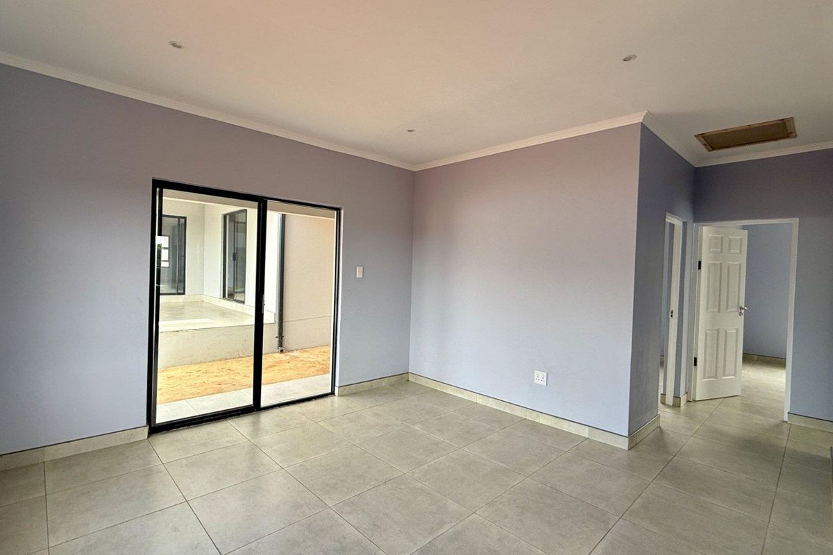 A bright, empty living room featuring neutral tiled flooring, recessed ceiling lighting, and a sliding glass door providing access to an outdoor patio area.