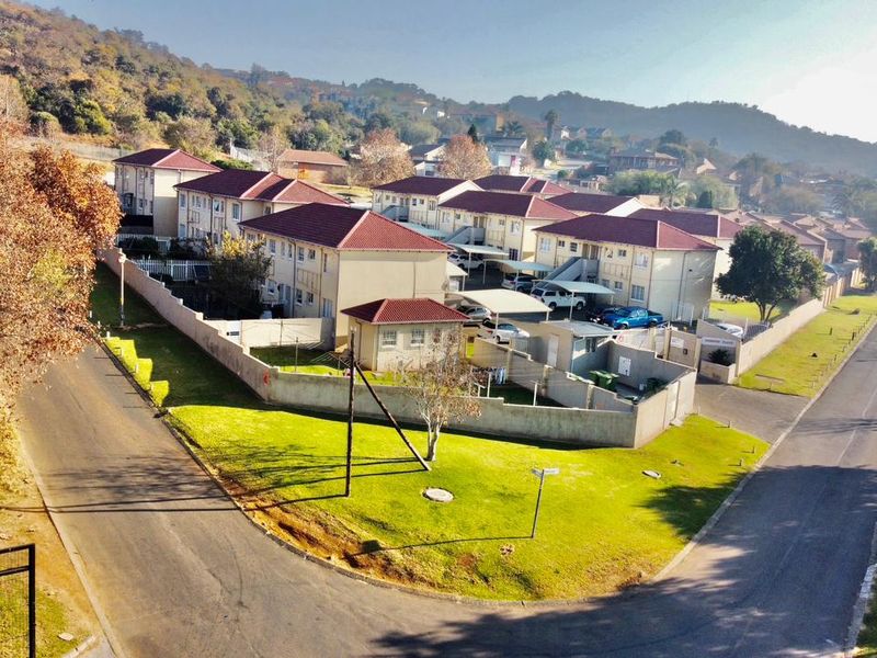 An aerial view of a residential apartment complex featuring multiple buildings with tiled roofs, paved driveways, and perimeter walling in a suburban setting.
