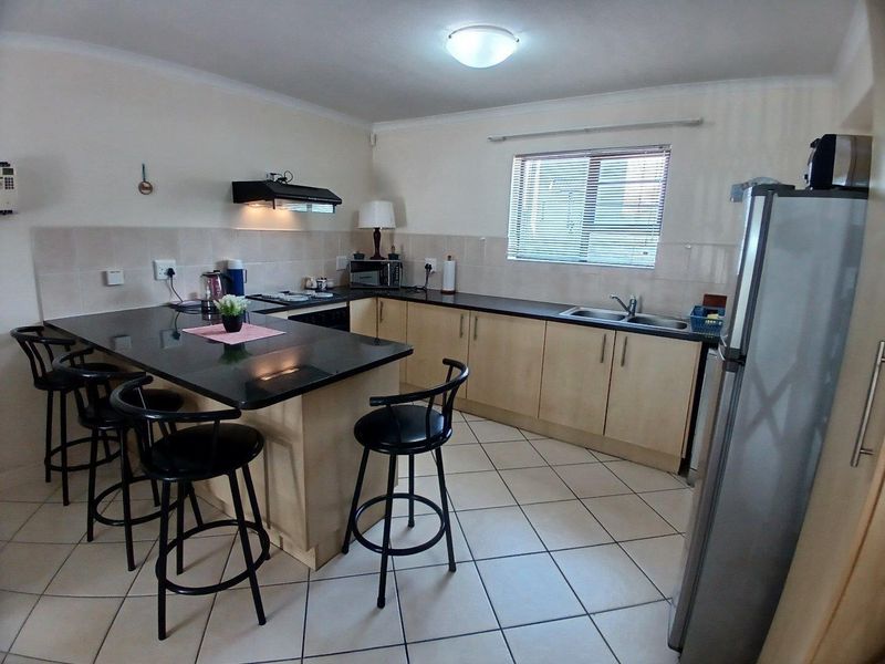 Functional kitchen featuring granite countertops, built-in cabinetry, a double basin sink, and tiled flooring with a breakfast bar area.