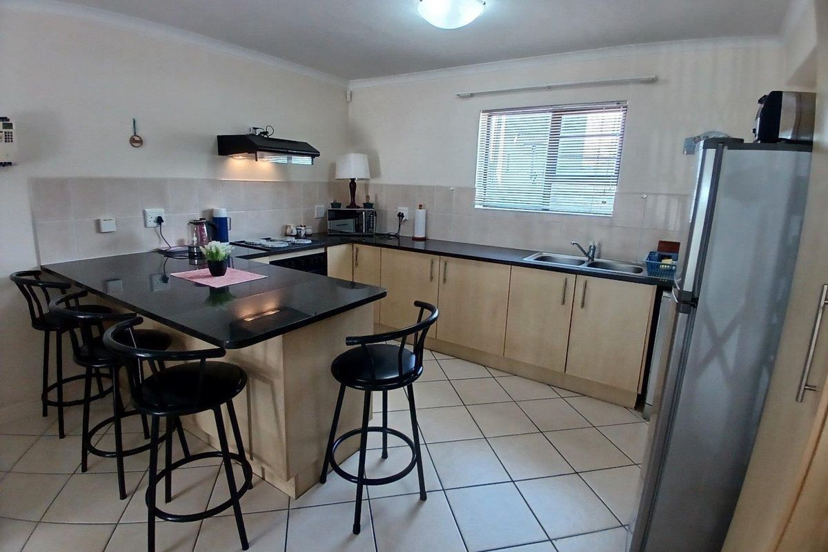 Functional kitchen featuring granite countertops, built-in cabinetry, a double basin sink, and tiled flooring with a breakfast bar area.